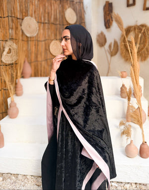 Woman in a black abaya with pink trim standing in a decorative indoor setting.