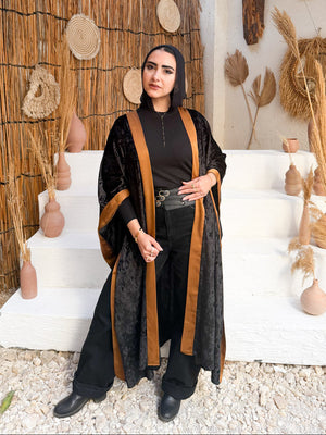 Woman in a black and brown outfit standing in a decorative outdoor setting with straw walls and decor.