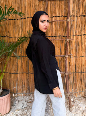 Person wearing a black hoodie and light gray pants standing in front of a reed wall.