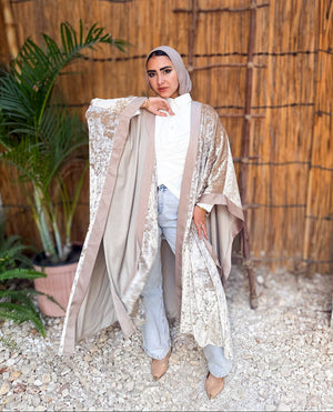 Woman wearing a beige embroidered cover-up in an outdoor setting with plants and a wooden wall.