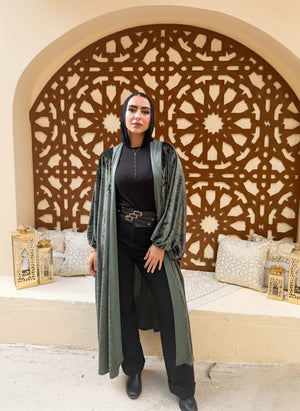 Woman in a long green coat standing in front of an ornate wall design.