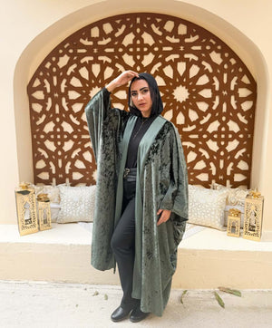 Woman in a green abaya standing in front of an ornate wooden screen.