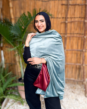 Woman holding a light blue wrap with a red interior against a wooden fence and plant background
