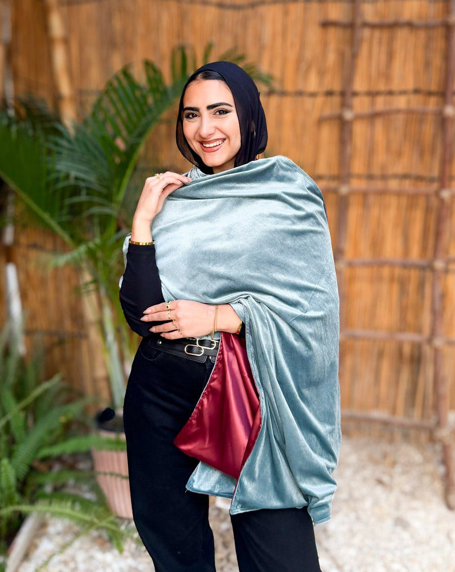 Woman holding a light blue wrap with a red interior against a wooden fence and plant background