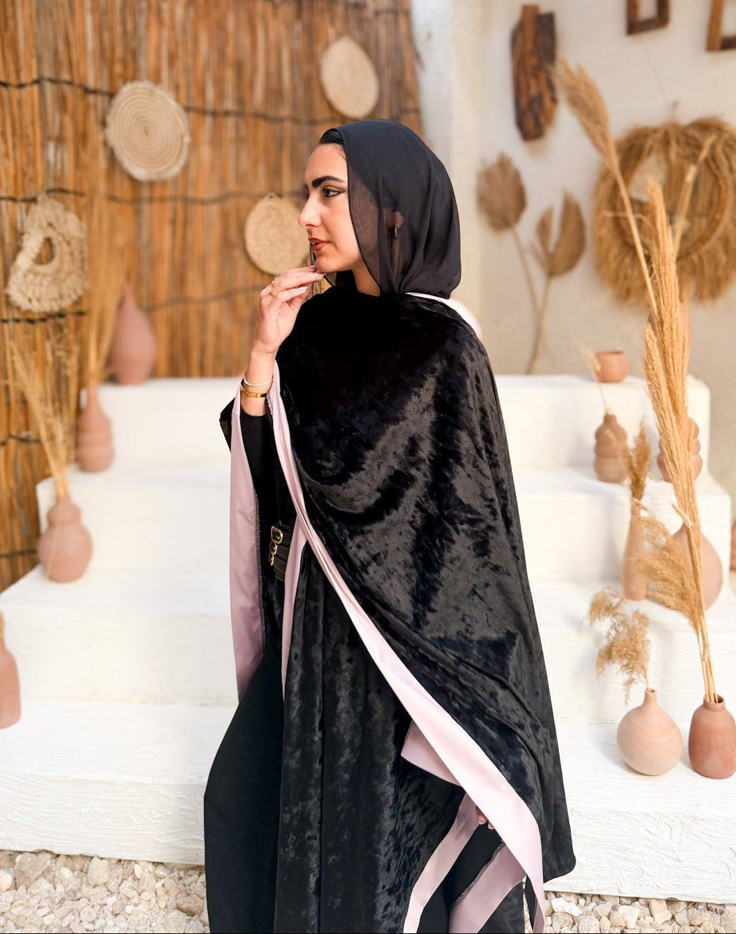 Woman in a black abaya with pink trim standing in a decorative indoor setting.