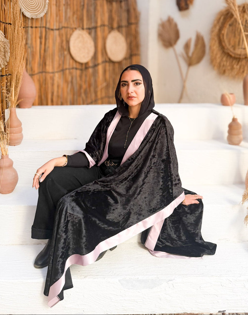 Woman in a black abaya sitting on a white couch with decorative elements in the background.