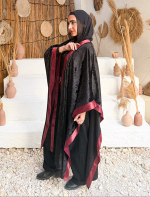Woman in a black and red traditional outfit standing in a rustic setting with wooden decor.