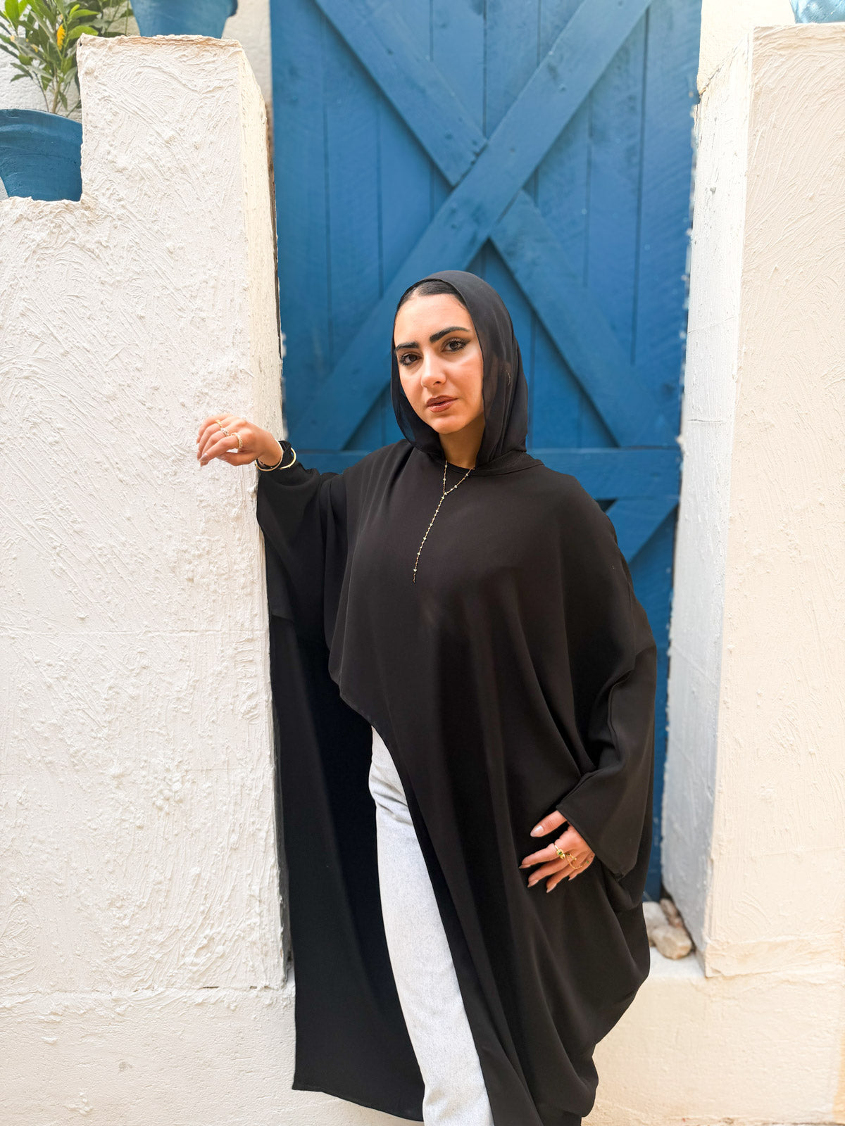 Woman in a black abaya standing against a blue door and white wall.