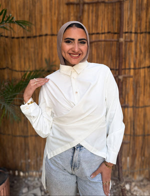 Woman wearing a white blouse and gray hijab standing against a woven wall.
