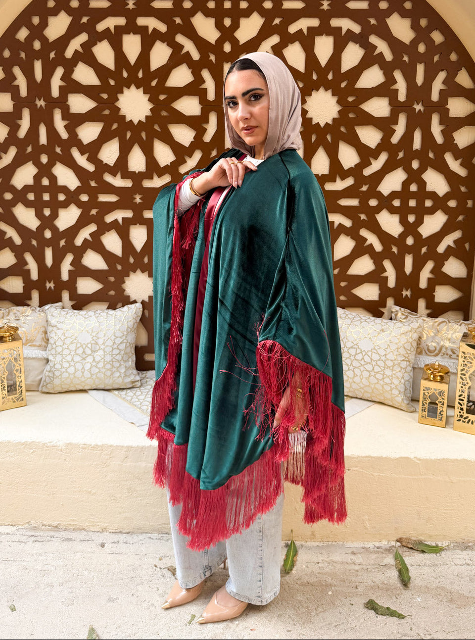 Woman wearing a teal and red shawl in a decorated room with an intricate wall design.