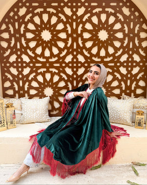 Woman in a green and red traditional outfit sitting in a decorated room with intricate wall patterns.