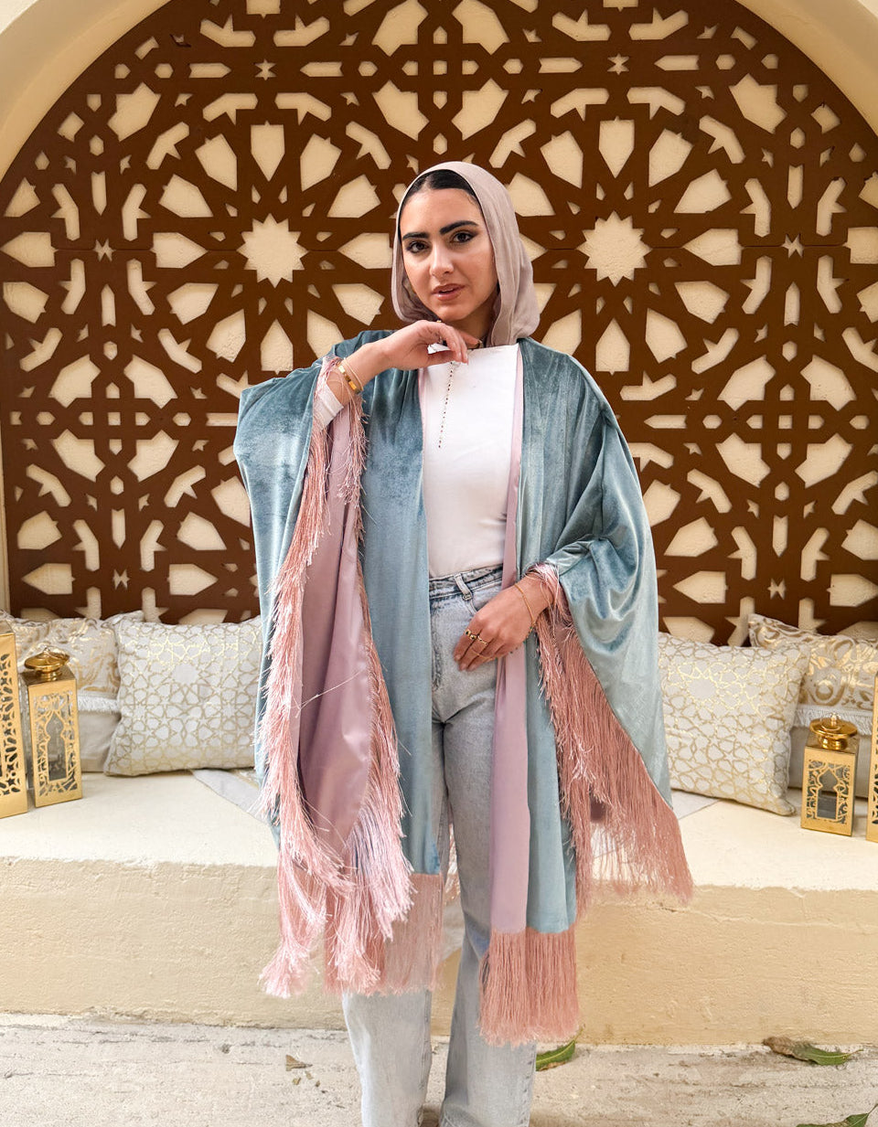 Woman in a light blue outfit with a pink scarf standing in front of an ornate wall design.