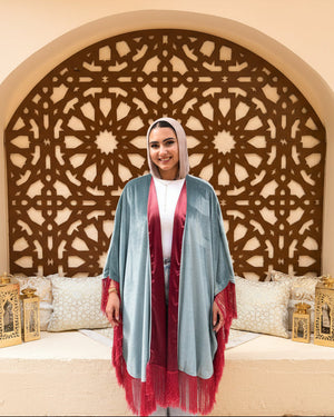 Woman wearing a light blue and red shawl in front of an ornate wall design.