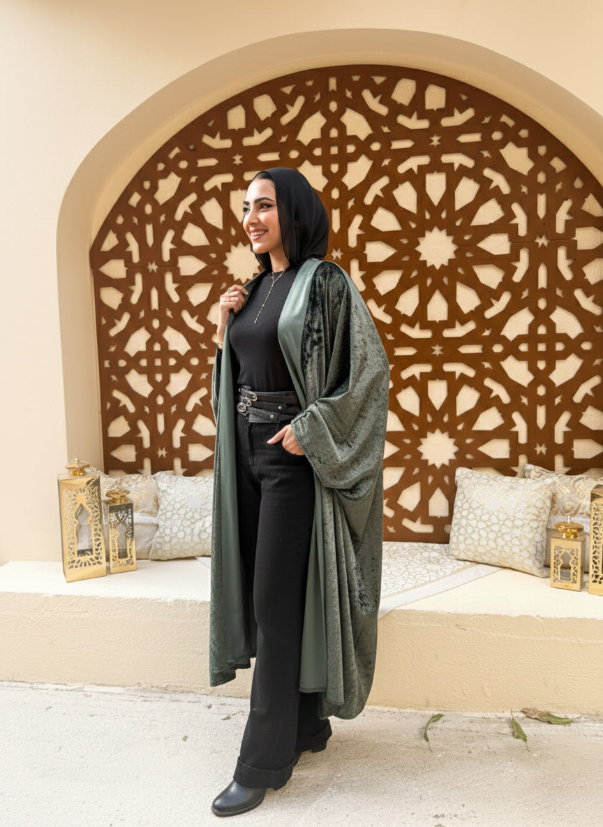 Woman wearing a long green coat over a black outfit in front of an ornate wall.