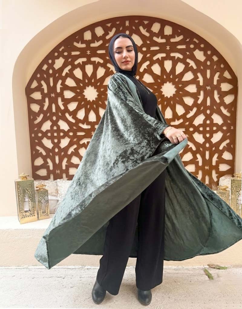 Woman holding a green velvet shawl in front of an ornate archway.